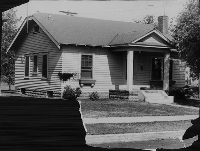 Torn black-and-white photograph of a white bungalow with columns supporting a front porch.